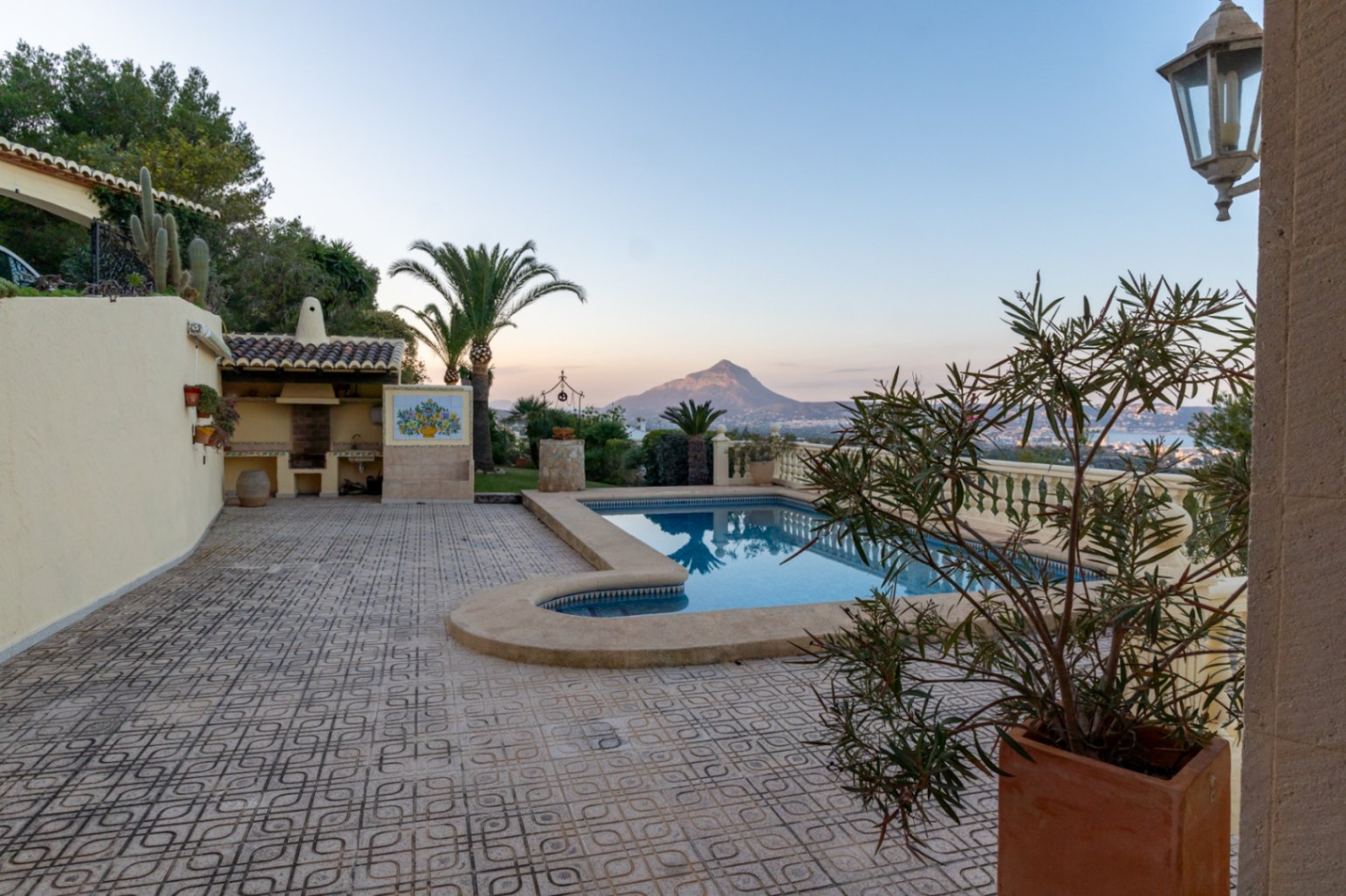 Terrace featuring a private pool, built-in outdoor kitchen, and panoramic views of the Montgó mountain and Jávea coastline at dusk.