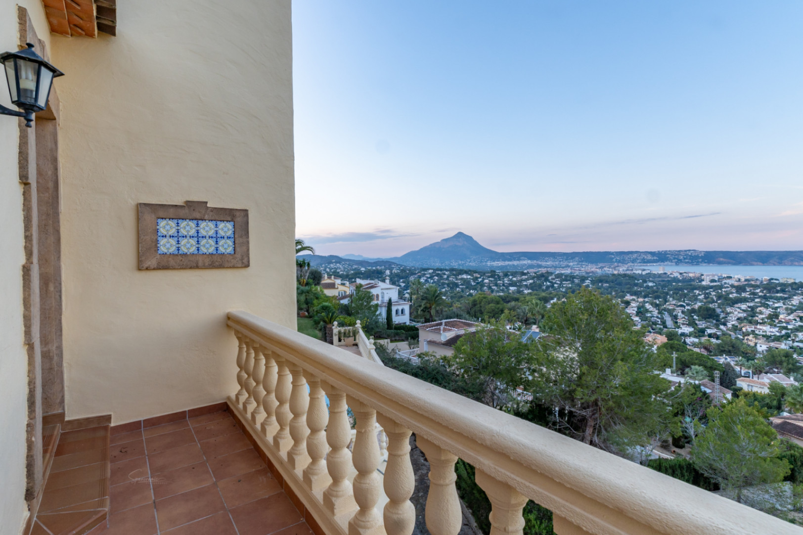 Terrace featuring terracotta tiles and a classic balustrade, overlooking the Montgó mountain and Jávea bay. A decorative ceramic tile panel accents the exterior wall.