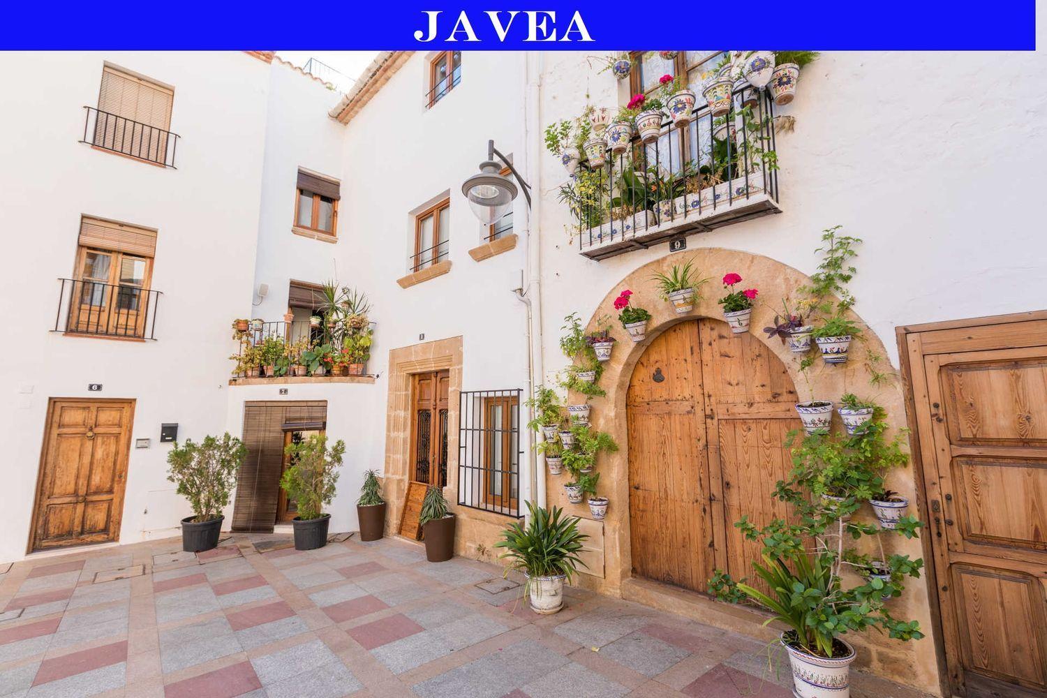 Traditional facade in Jávea's old town featuring wooden doors, tosca stone arches, and decorative ceramic flower pots on whitewashed walls.