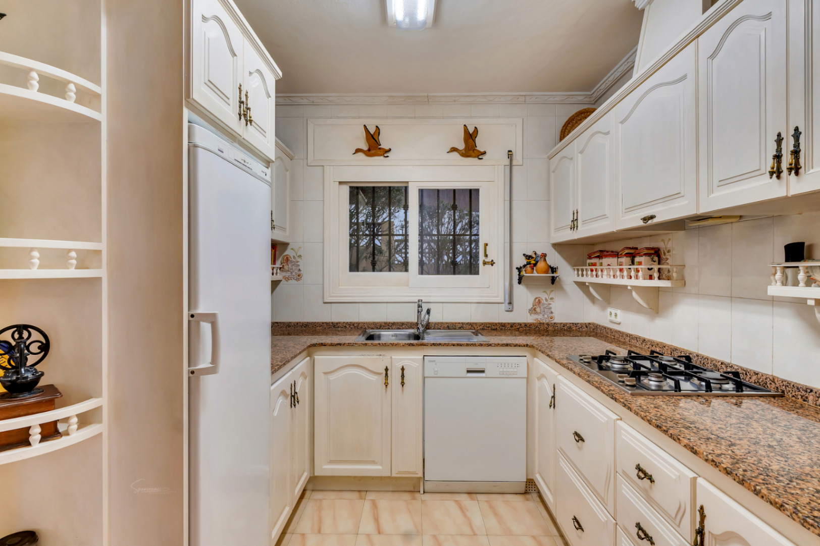 Traditional kitchen featuring white cabinetry, granite countertops, a gas cooktop, and an integrated dishwasher positioned under a window for natural light.