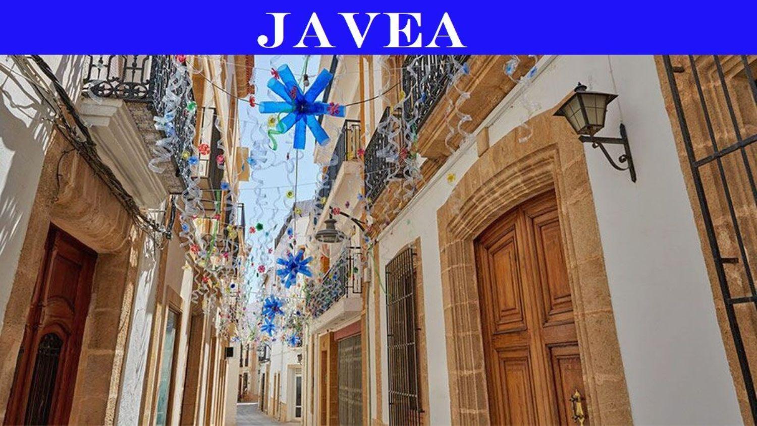 Traditional narrow street in Jávea's old town featuring Tosca stone door frames, wrought iron balconies, and festive overhead decorations.