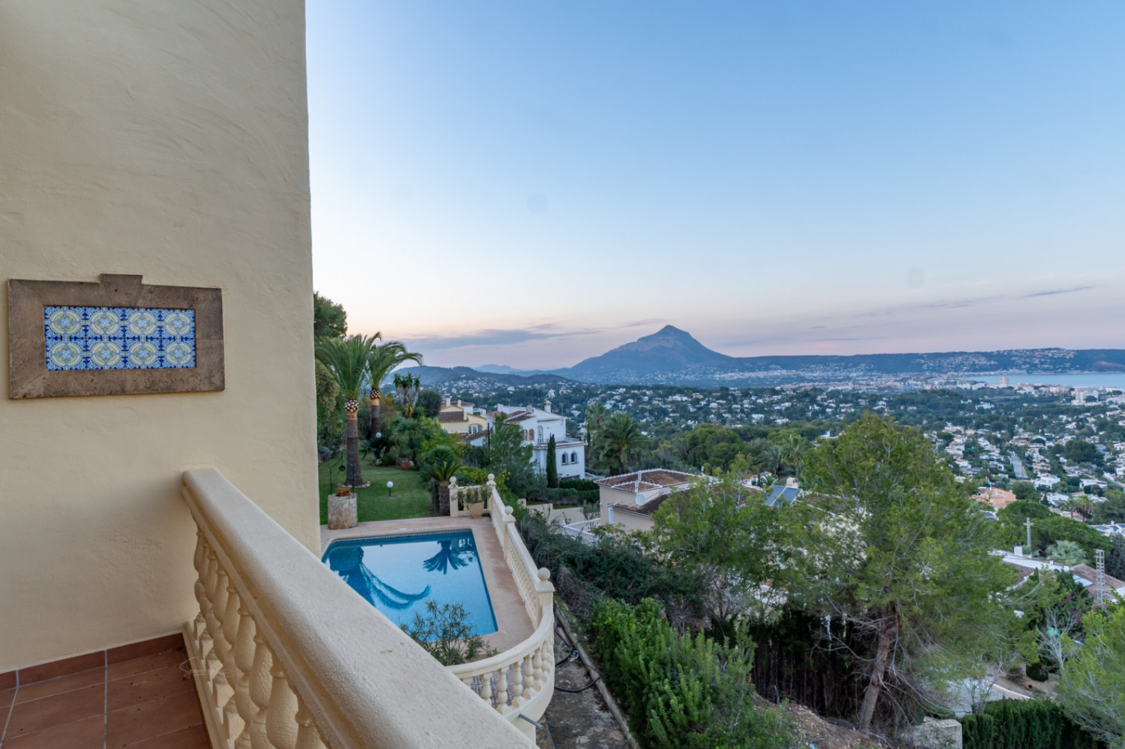 Upper terrace featuring stone balustrades and decorative tiling, overlooking the private pool, Mediterranean garden, and panoramic views of the Montgó and Jávea bay.
