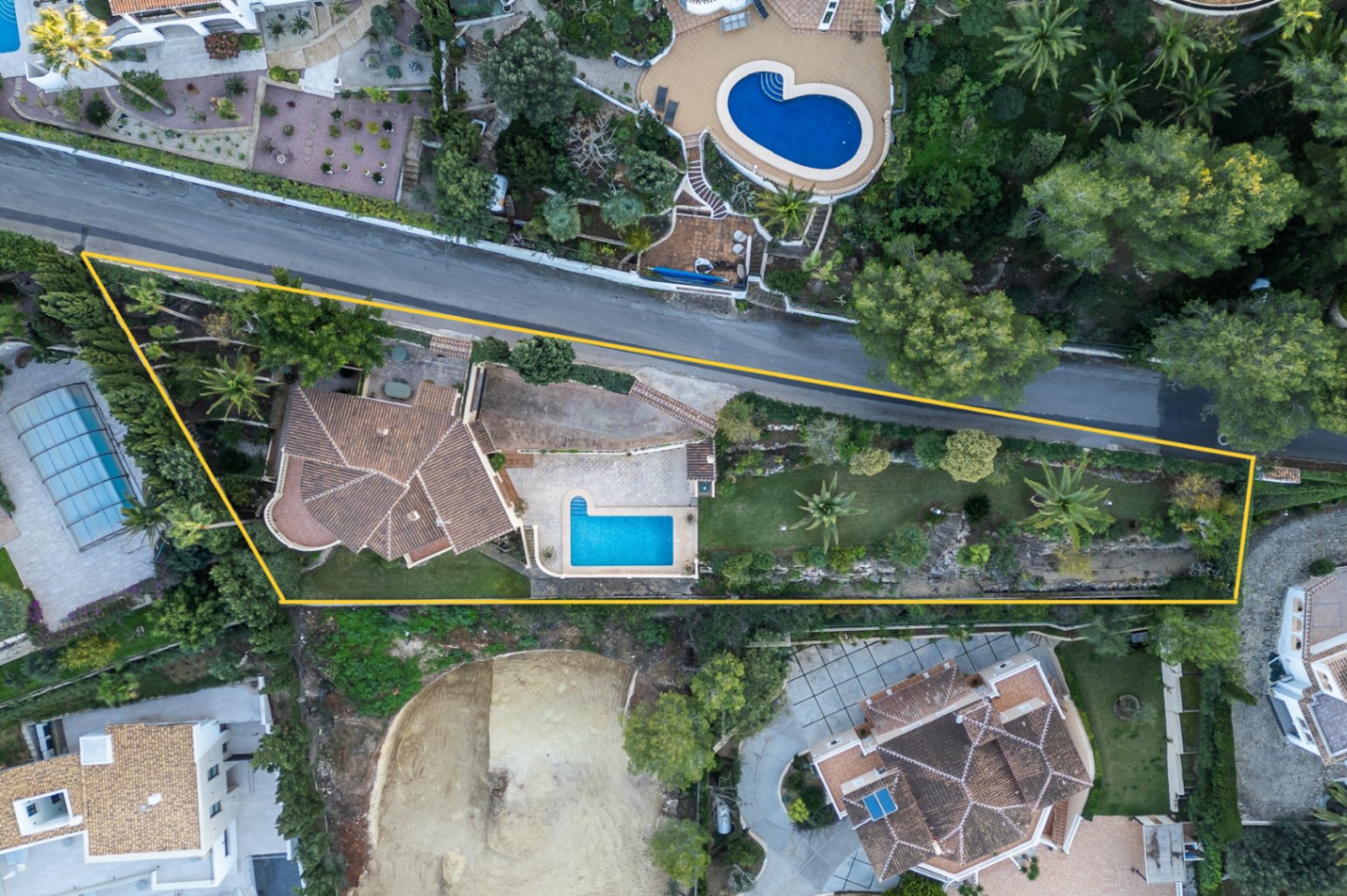 Zenithal aerial view of the property plot, highlighting the villa's layout, the swimming pool, Mediterranean gardens with palms, and the private driveway.