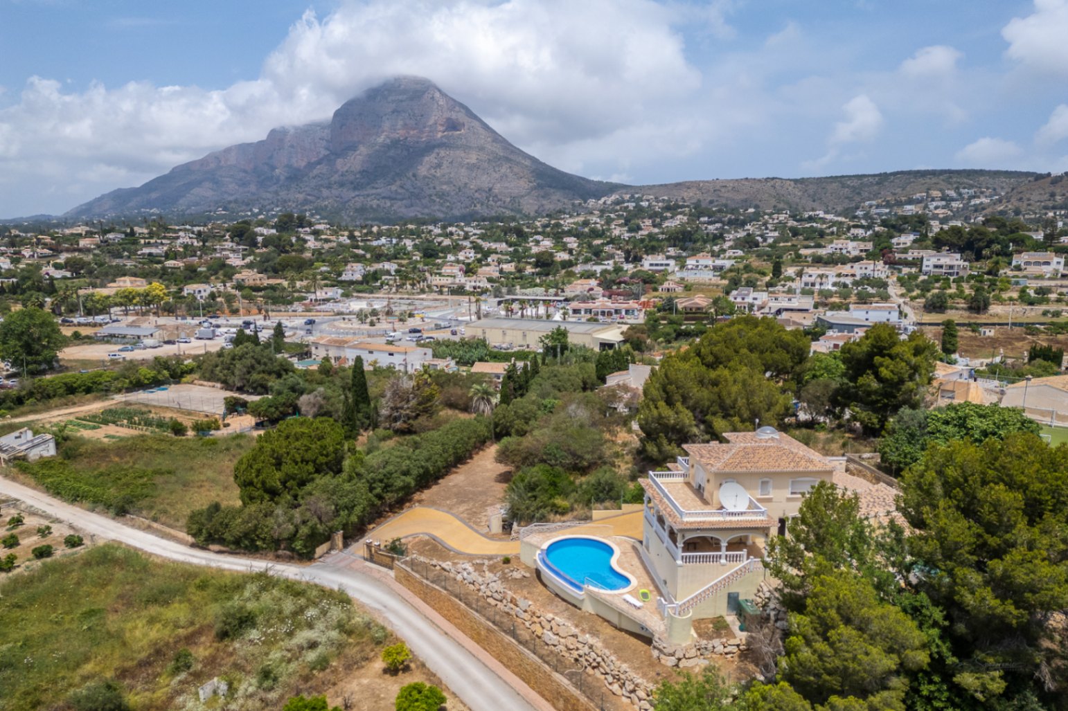 Aerial perspective of the villa showcasing the elevated curved pool and terraces with expansive views of the valley and the Montgó mountain.
