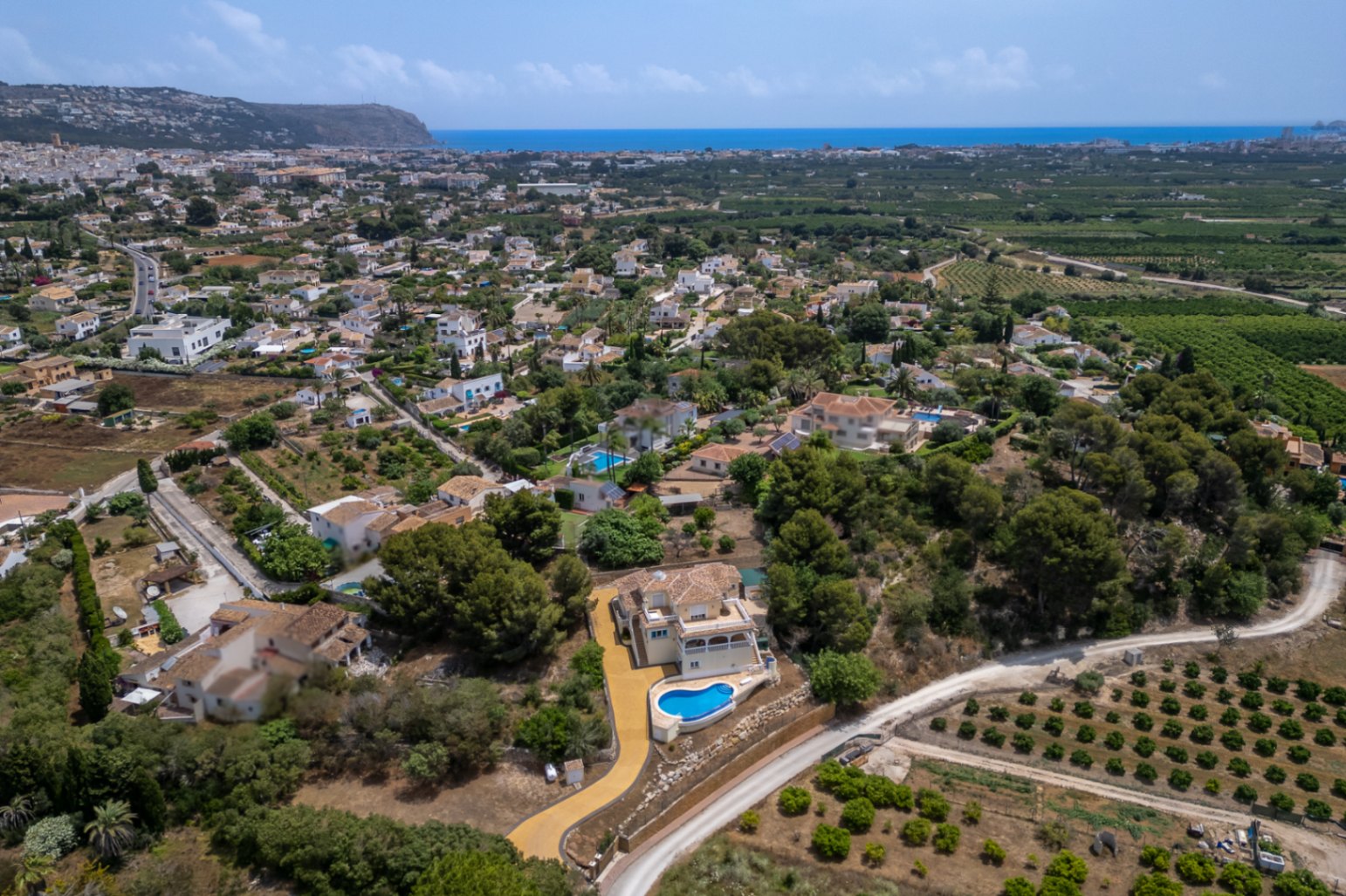 Aerial view of the villa featuring its elevated position, infinity pool, and expansive driveway, offering panoramic views across the Jávea valley to the Mediterranean Sea.