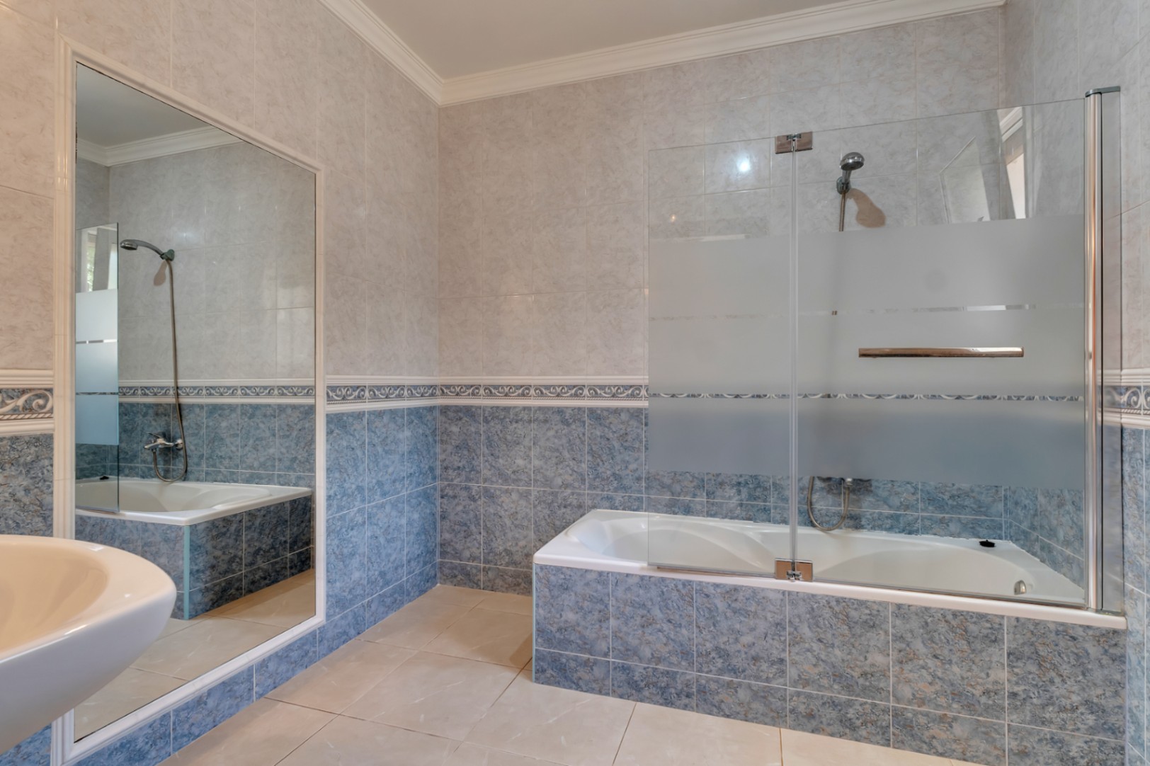 Bathroom featuring a built-in bathtub with a glass screen, blue patterned wall tiles with decorative borders, and a large wall-mounted mirror.
