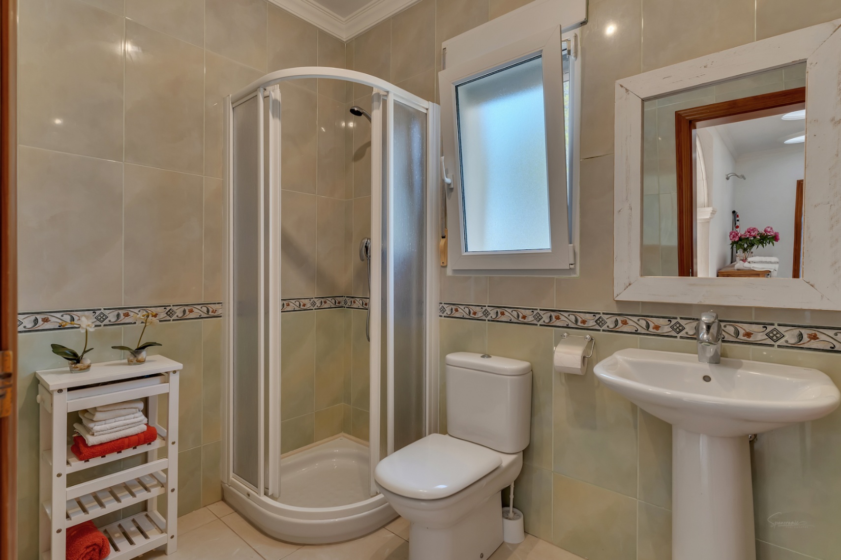 Bathroom featuring a curved corner shower enclosure, white pedestal sink, and tiled walls with a decorative horizontal border.