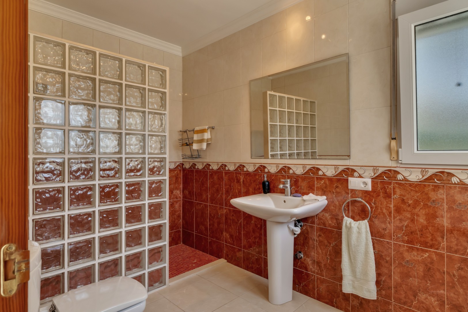 Bathroom featuring a pedestal sink, a large wall mirror, and a walk-in shower separated by a glass block partition and decorative red marble-effect tiling.