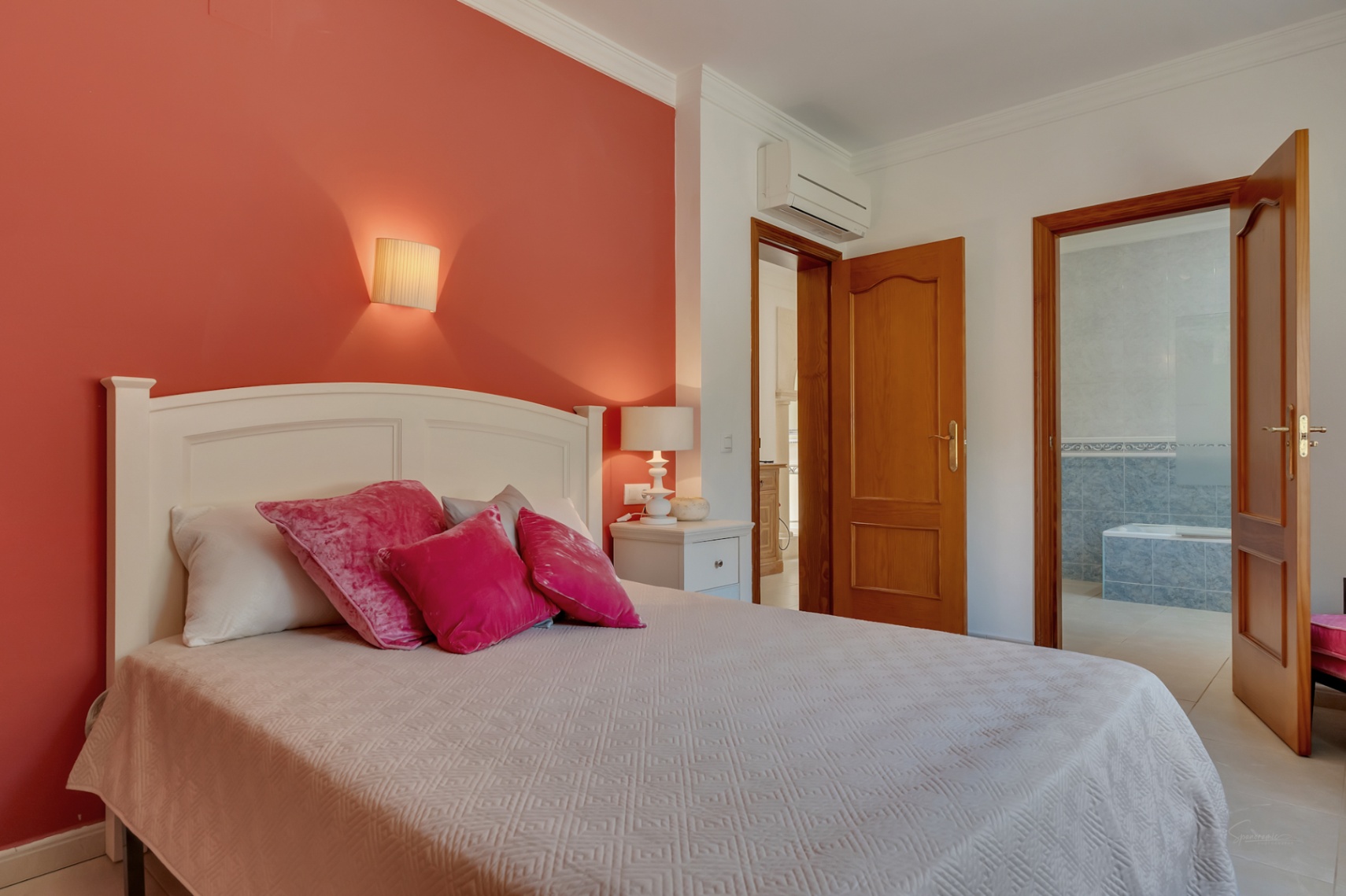 Bedroom featuring a terracotta accent wall, split-system air conditioning, and an en-suite bathroom with blue tiling and a built-in bathtub.