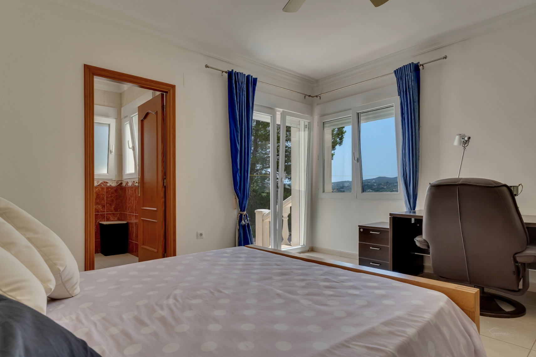 Bright bedroom featuring direct terrace access, an integrated workspace, and an en-suite bathroom with distinctive reddish marble tiling.