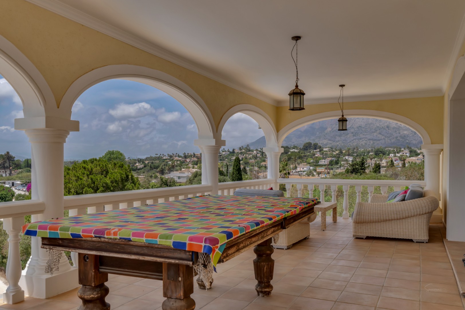 Covered arched terrace featuring a billiard table, lounge seating, and expansive 180-degree views of the surrounding valley and Montgó mountain.