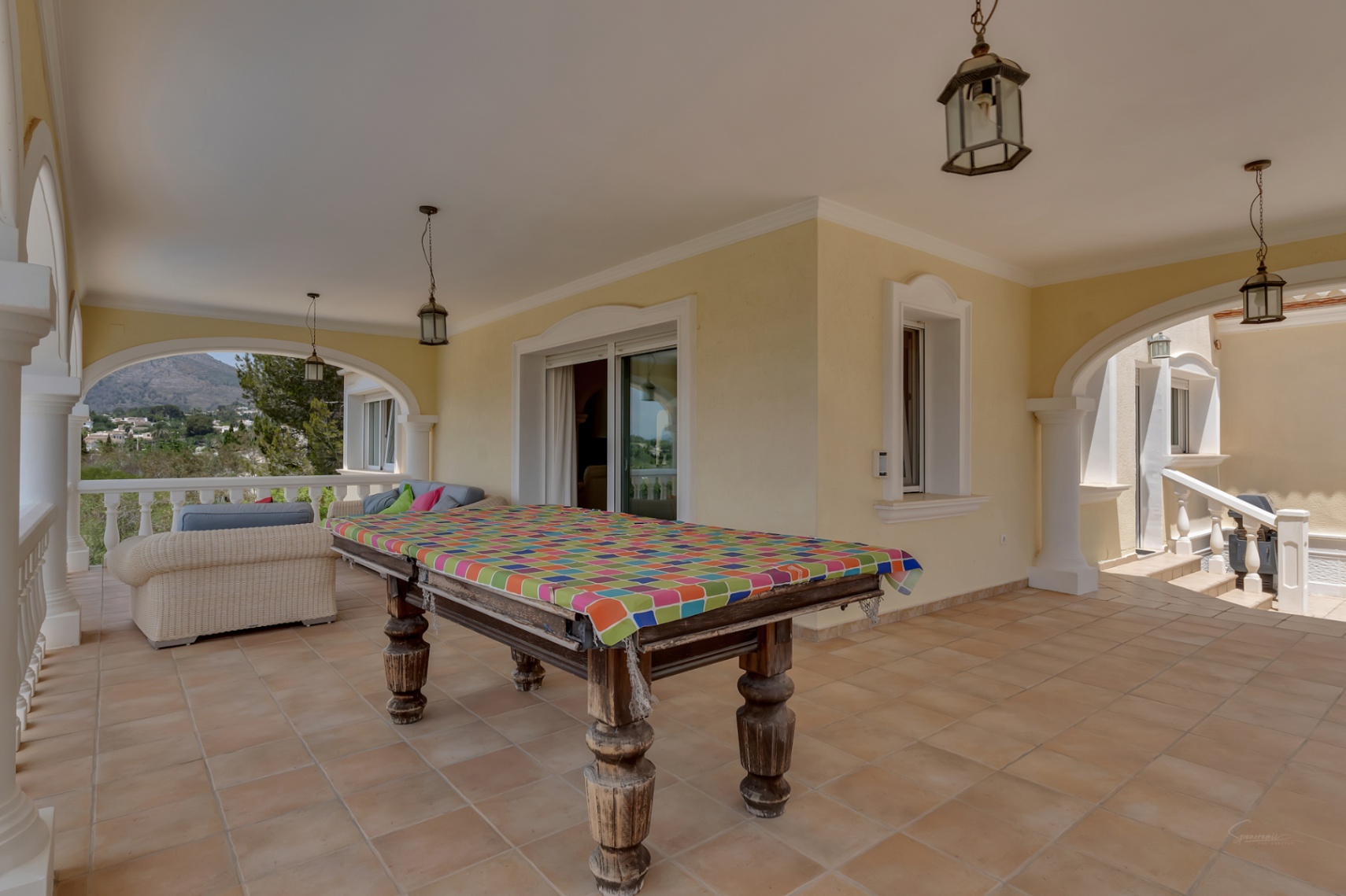 Covered terrace featuring traditional arches, terracotta flooring, and a central billiard table. It offers panoramic valley views and includes a wicker lounge area.