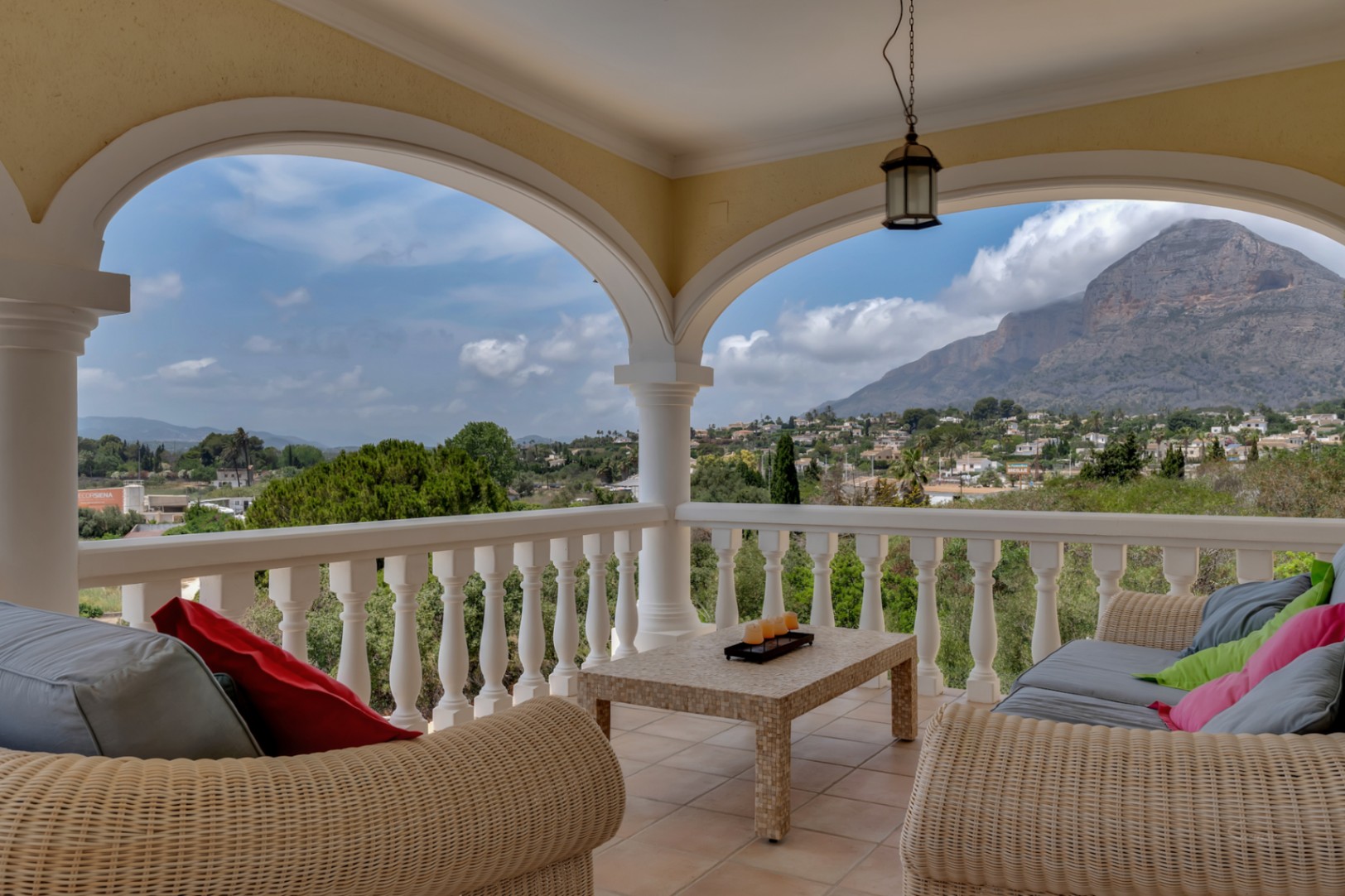 Covered terrace featuring traditional arches, wicker lounge seating, and panoramic views of the Montgó mountain and surrounding valley.