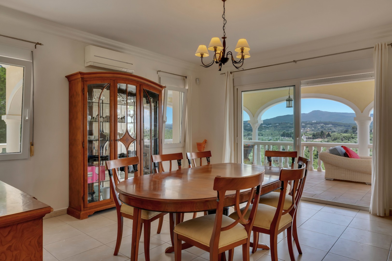 Dining room featuring an oval wooden table, a classic display cabinet, and sliding doors opening to a covered terrace with expansive valley views.