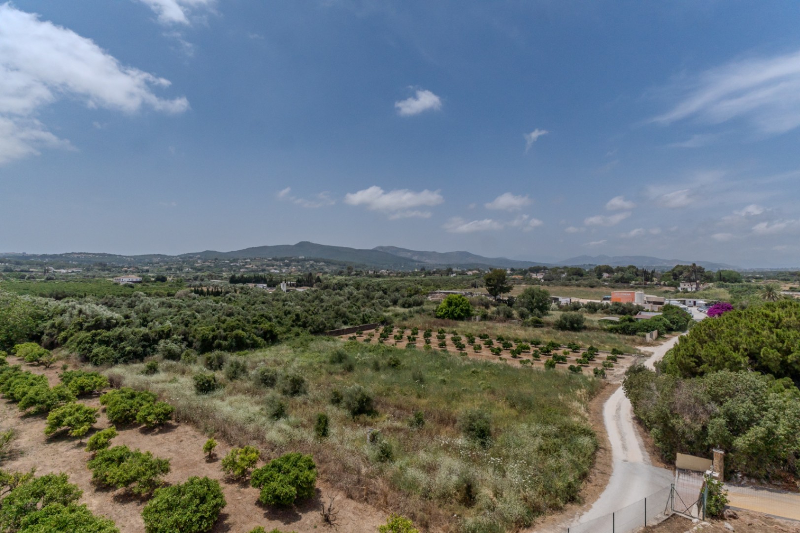 Elevated 180-degree panoramic view overlooking the lush Jávea valley, featuring agricultural orchards and the distant Benitachell mountain range.