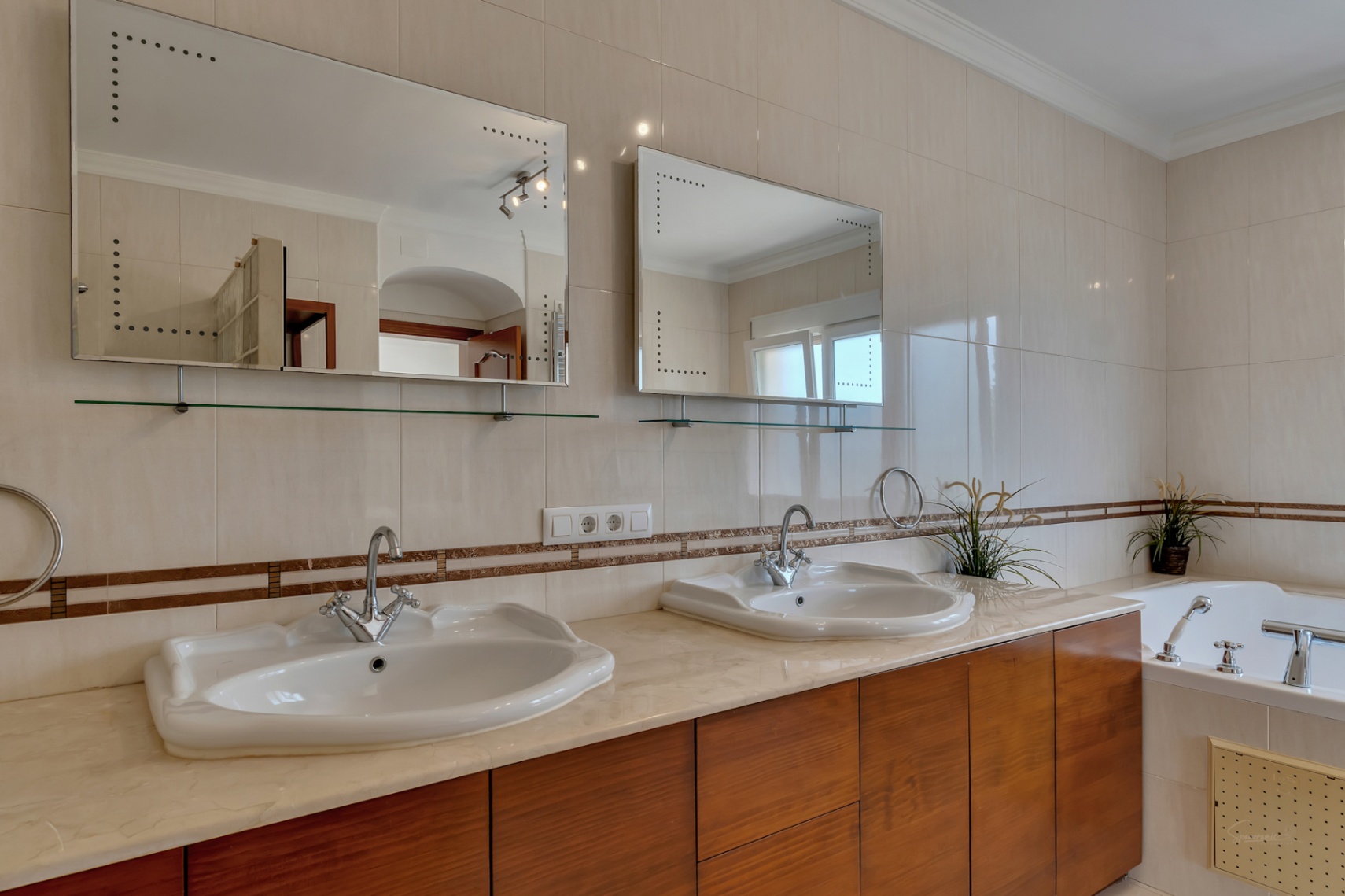 En-suite bathroom featuring a double vanity with marble countertop, wooden cabinetry, and backlit mirrors adjacent to the hydromassage tub.
