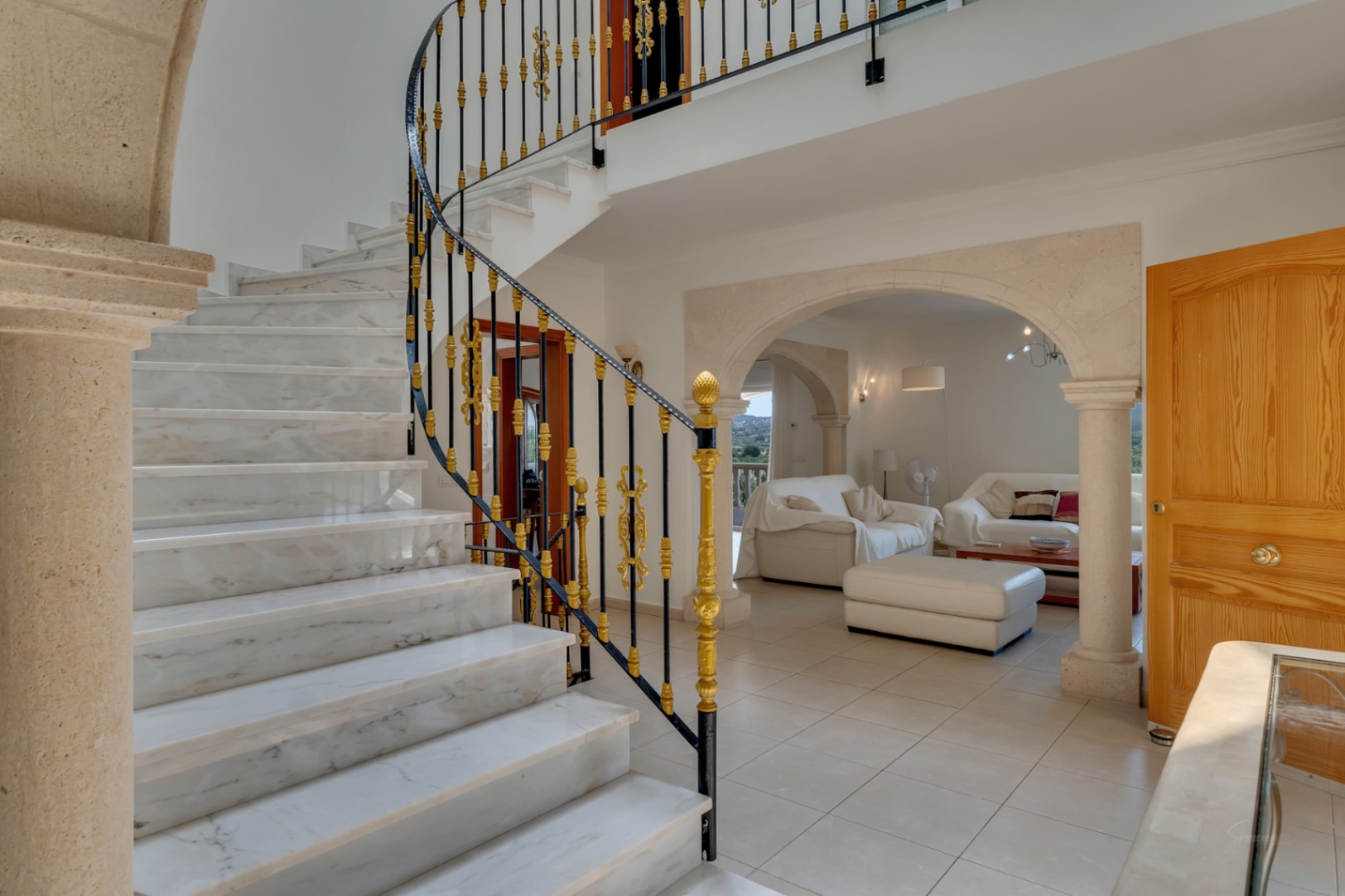 Entrance hall featuring a marble staircase with ornate wrought iron railings. Natural stone arches lead to the living area, showcasing a blend of traditional and elegant materials.
