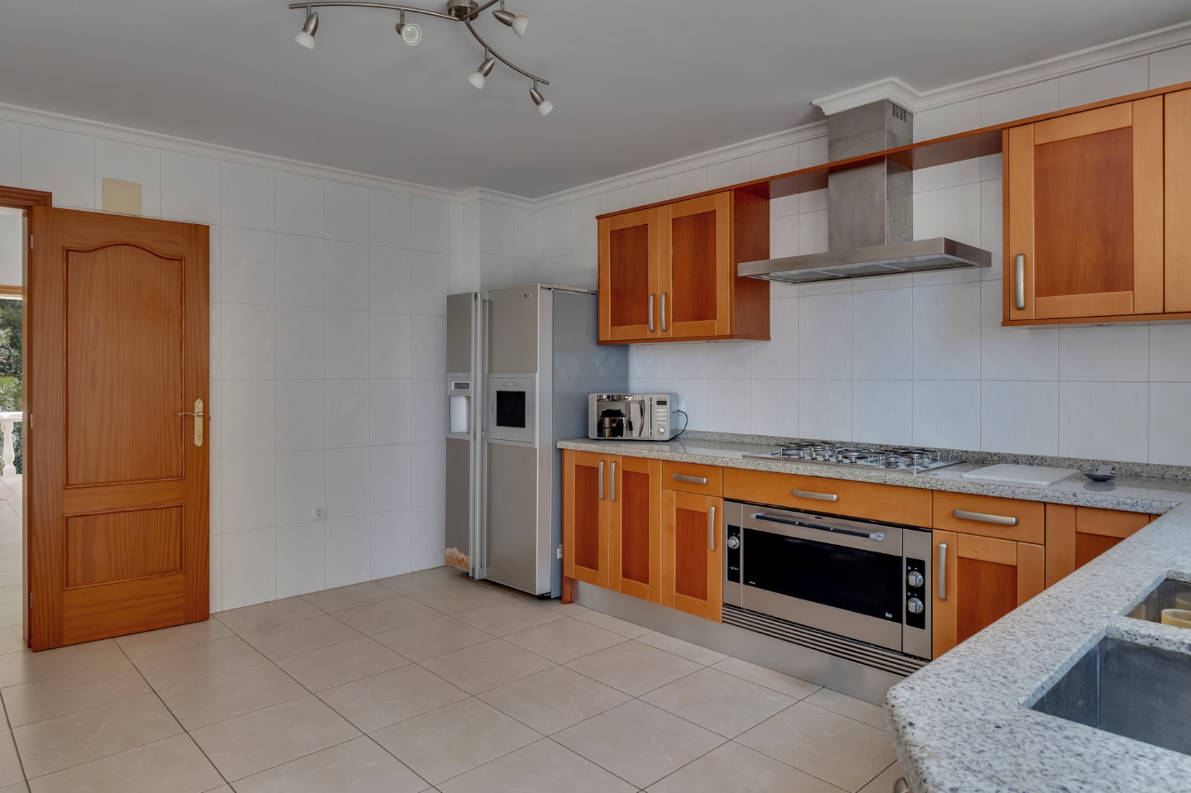 Fully equipped kitchen featuring wooden cabinetry, grey granite countertops, and stainless steel appliances, including a double American-style refrigerator and wide oven.