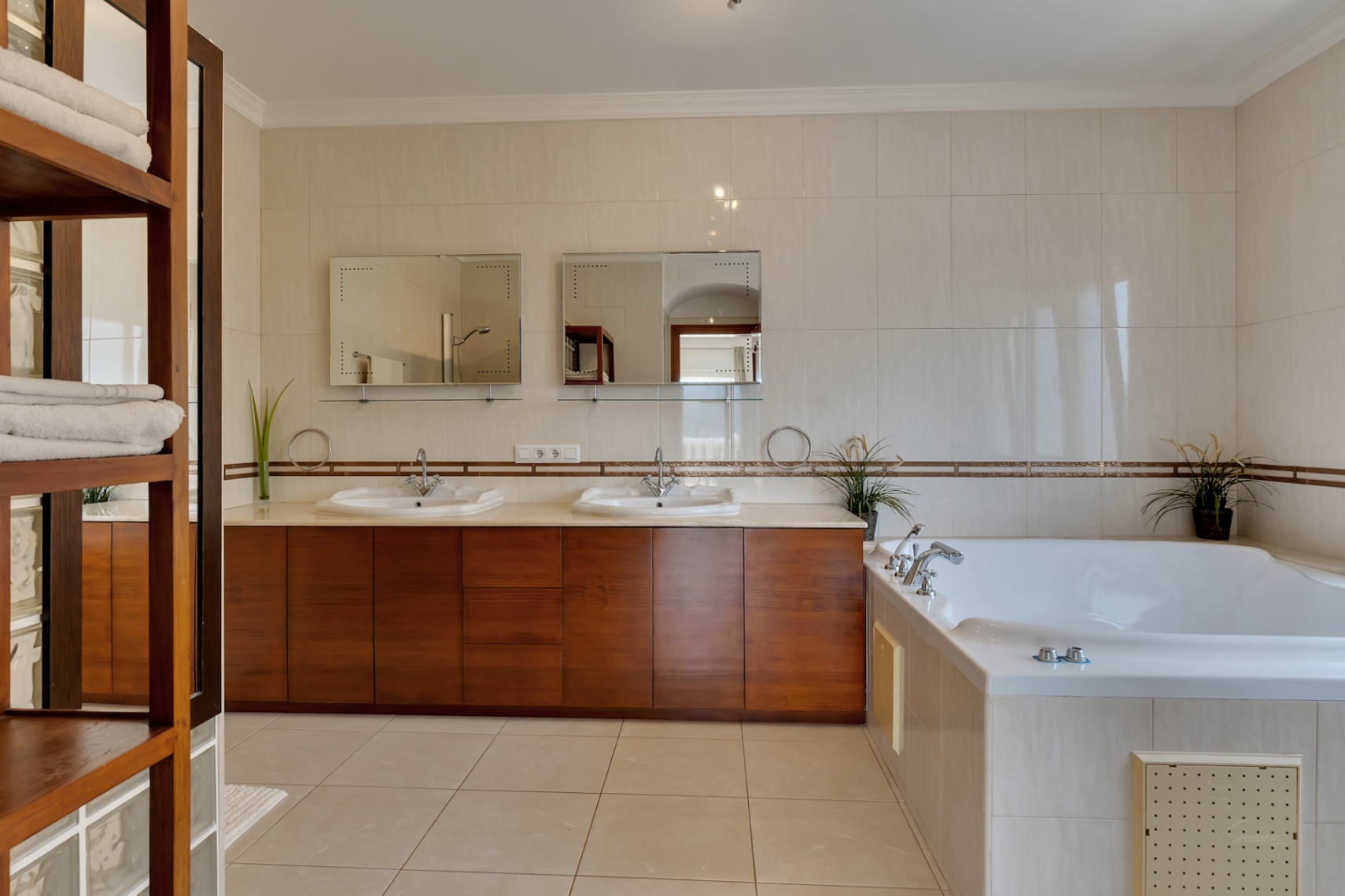 Master bathroom featuring a double wooden vanity, twin mirrors, and a large built-in hydromassage bathtub surrounded by neutral tiling.
