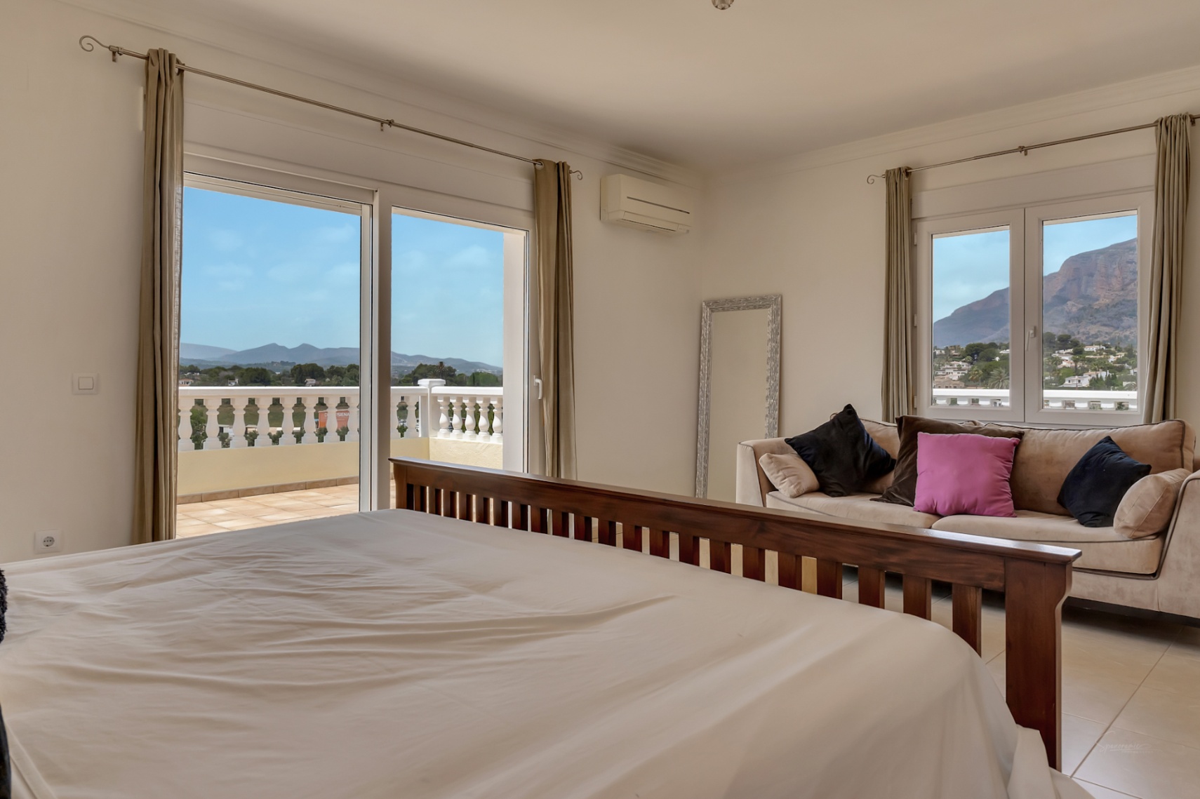 Master bedroom featuring a dark wood bed frame, integrated seating area, and sliding doors opening to a terrace with panoramic mountain and valley views.