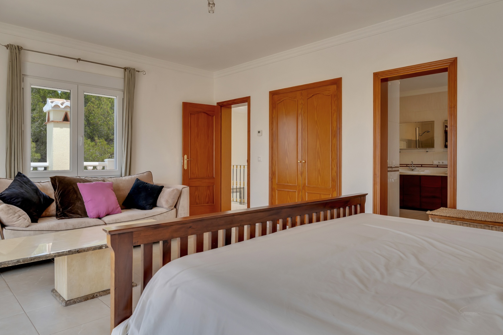Master bedroom featuring a seating area, built-in wooden wardrobes, and an ensuite bathroom. The space includes tiled flooring and views of the greenery.