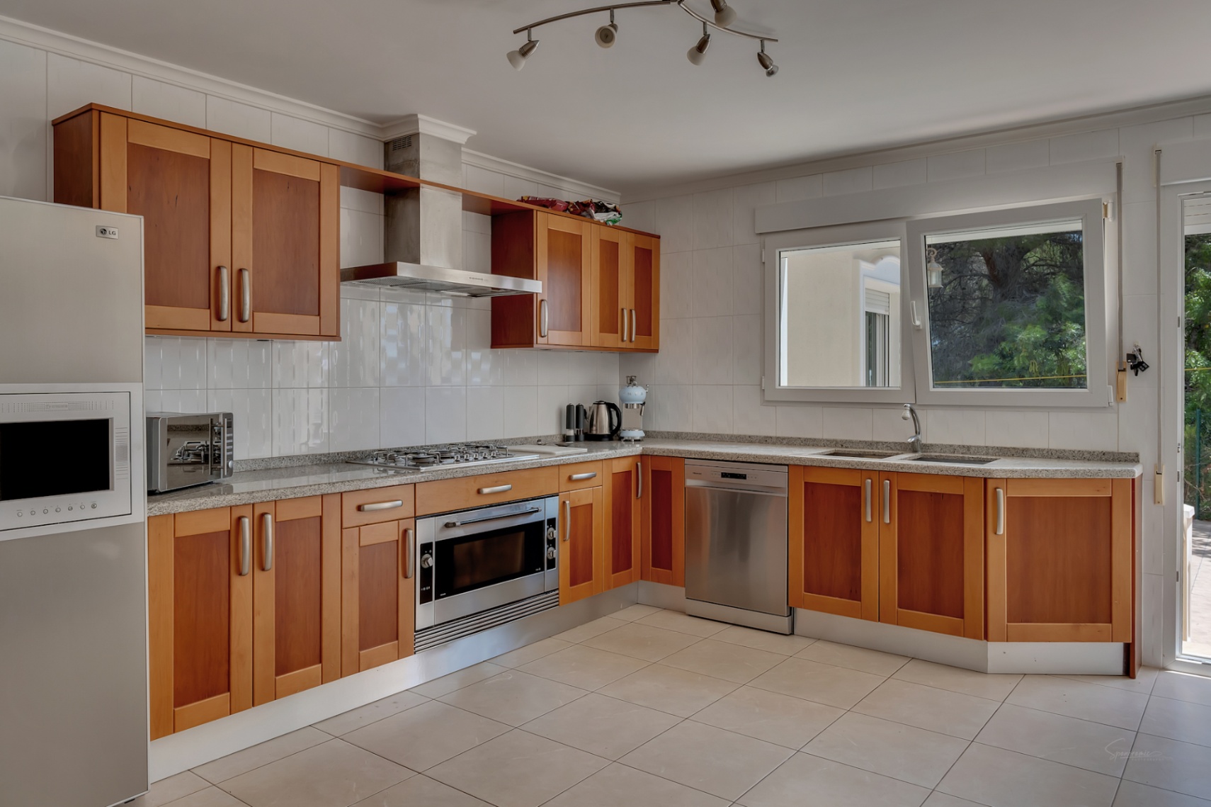 Spacious kitchen featuring wooden cabinetry, granite countertops, stainless steel appliances, and a large window for natural light.