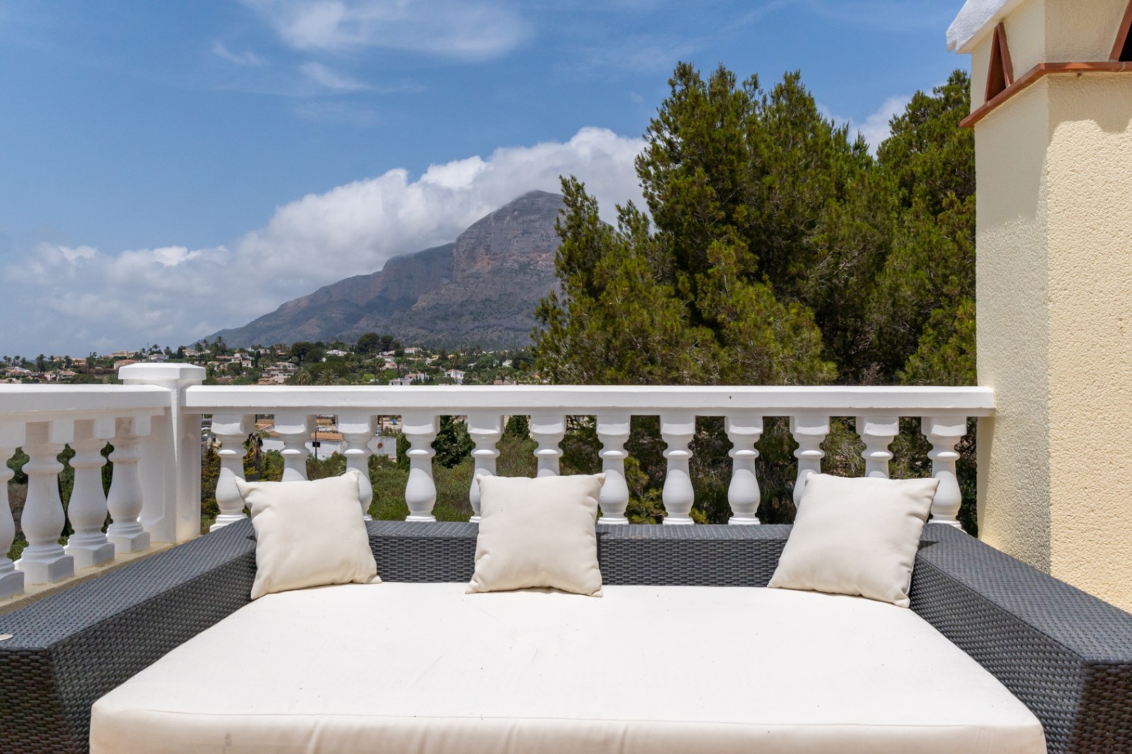 Upper terrace featuring a large rattan daybed and classic white balustrade, offering clear views of the Montgó mountain and surrounding landscape.