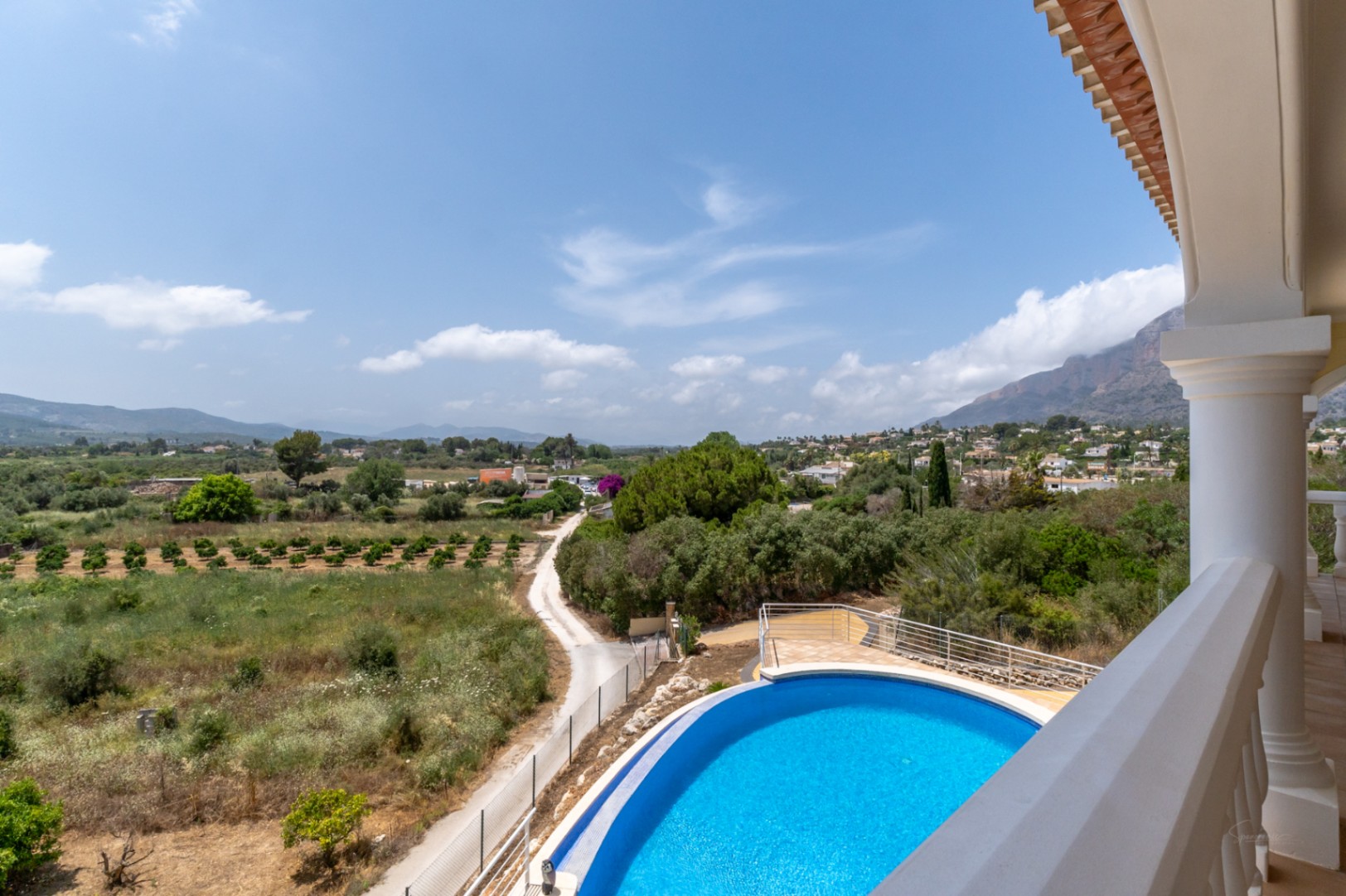 View from the upper terrace featuring the curved infinity pool and 180-degree panoramic vistas across the Jávea valley towards Mount Montgó.