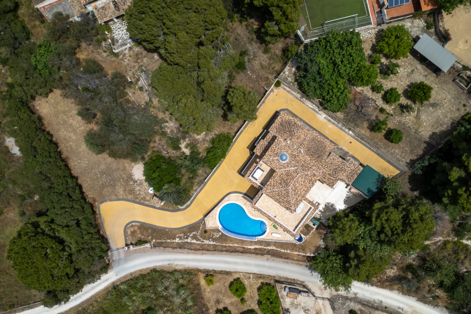 Zenith aerial view of the villa highlighting the plot layout, tiled roof with central dome, curved driveway, and integrated swimming pool.