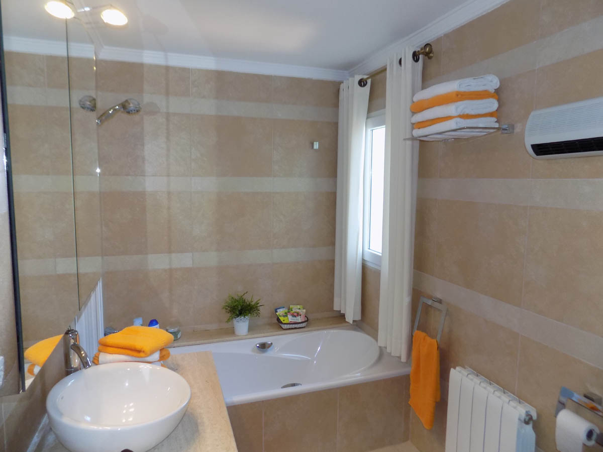 Bathroom featuring a built-in bathtub, a white vessel sink on a stone countertop, and walls finished in cream-toned tiles with horizontal stripes.