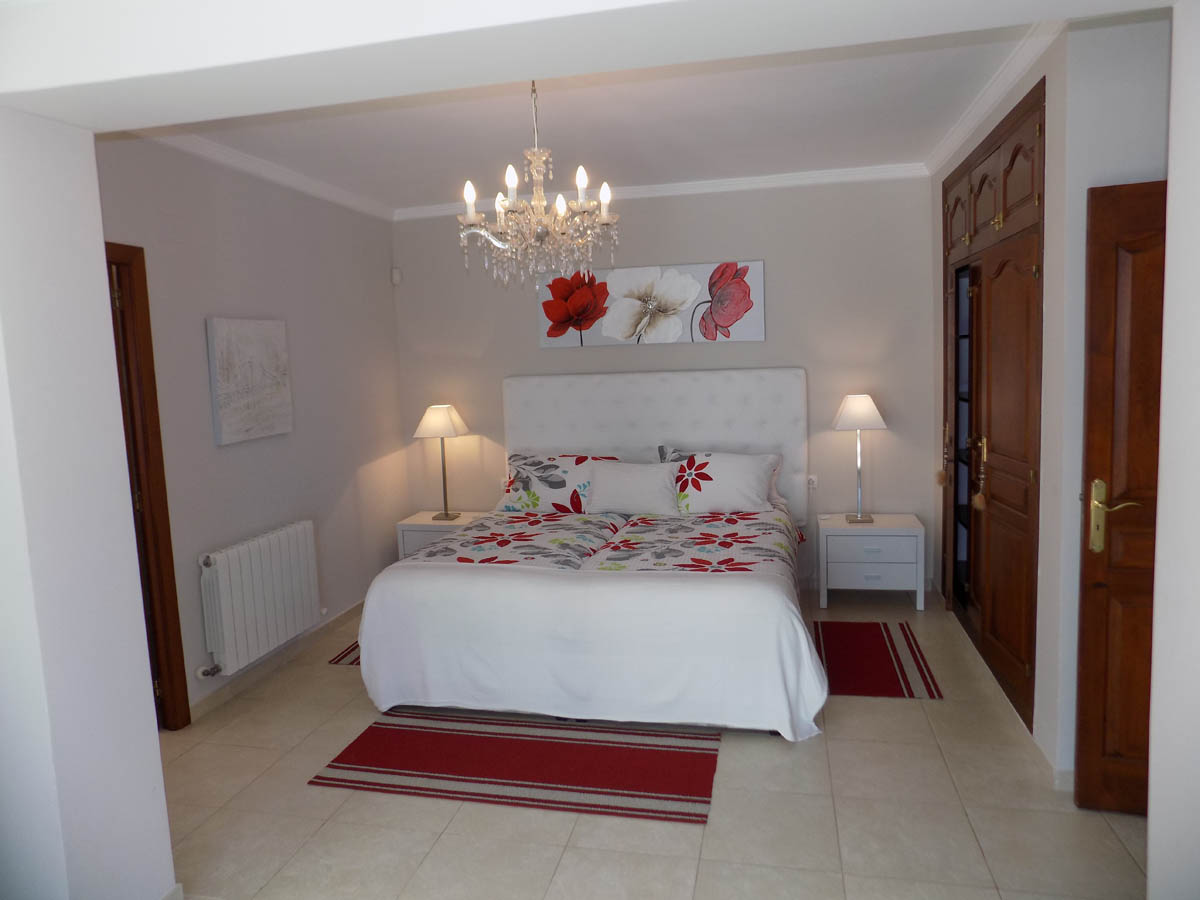 Bedroom featuring built-in wooden wardrobes, a white tufted headboard, crystal chandelier lighting, and tile flooring with radiator heating.