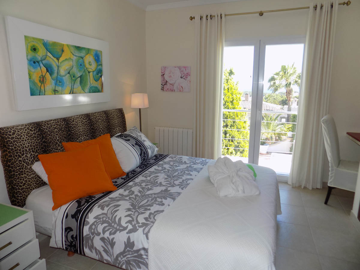 Bright bedroom featuring direct terrace access, a double bed with leopard print headboard, and natural light highlighting views of the Mediterranean garden.