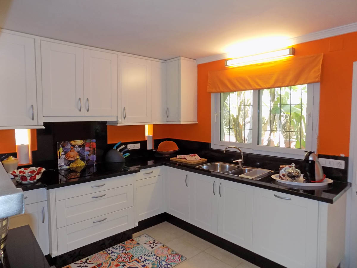 Fully equipped kitchen featuring white shaker cabinets, black granite countertops, and vibrant orange walls. Includes a double stainless steel sink and garden views.