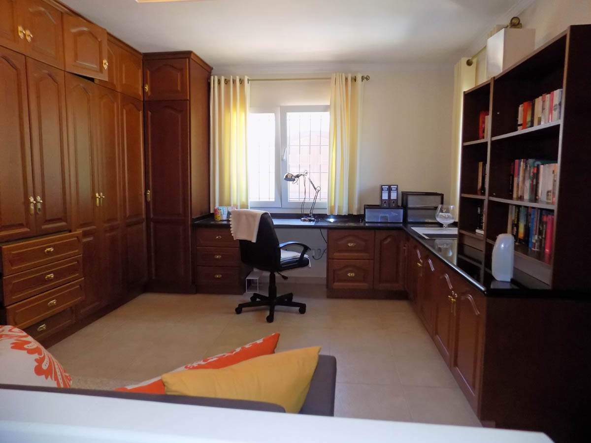 Functional home office featuring extensive built-in wooden cabinetry, an L-shaped desk with a dark countertop, and integrated bookshelves.