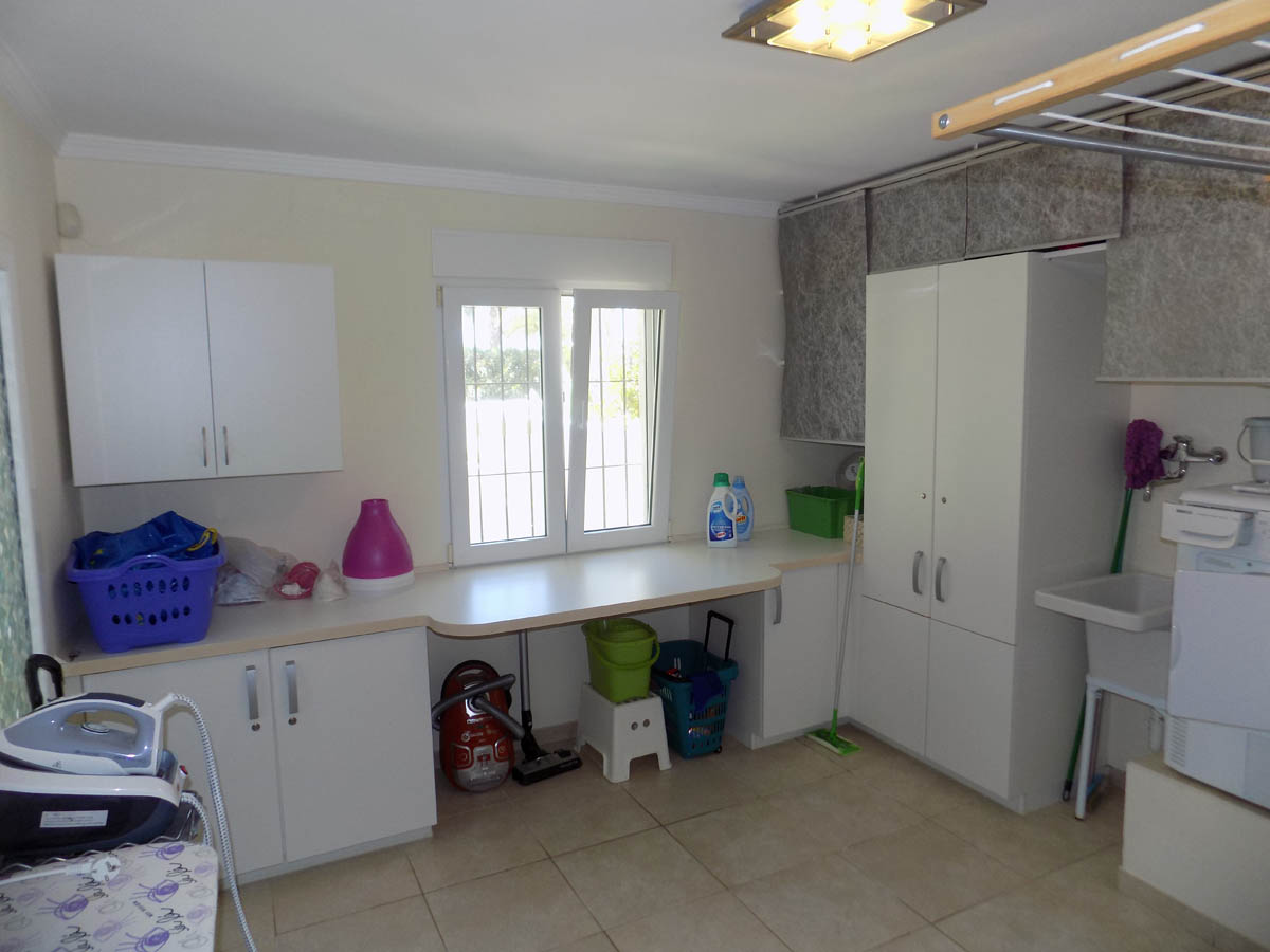 Functional laundry room featuring white cabinetry, a large countertop, utility sink, and natural light from a window. Designed for efficient home management.