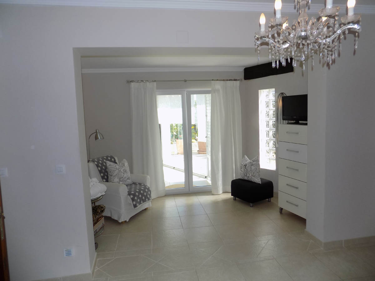 Master bedroom with a dedicated sitting area, geometric tiled flooring, and terrace access. Features a white dresser and natural light from glass block windows.