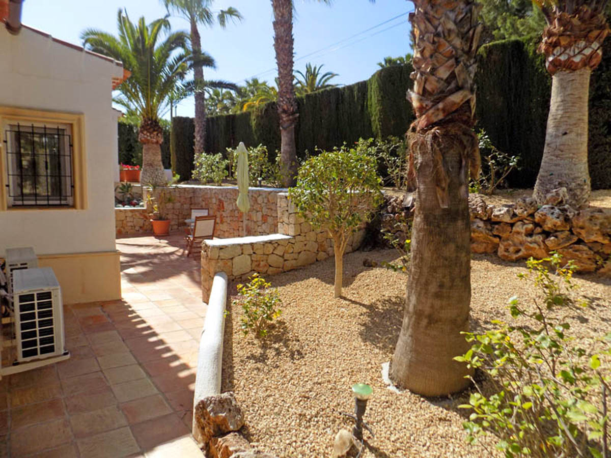 Mediterranean garden featuring mature palm trees, natural stone walls, and terracotta tiling. Low-maintenance landscaping with gravel and high hedges ensures privacy.