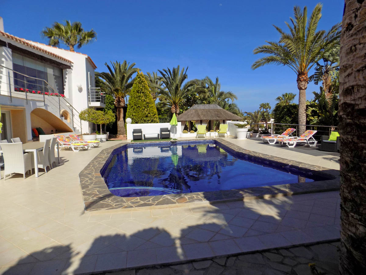 Outdoor swimming pool with stone edging, spacious tiled terrace featuring dining furniture, sun loungers, and a thatched chill-out hut.