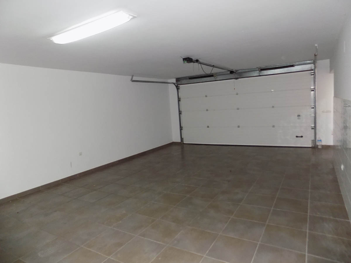 Spacious double garage featuring tiled flooring, white walls, and an automatic sectional overhead door with a ceiling-mounted motor.
