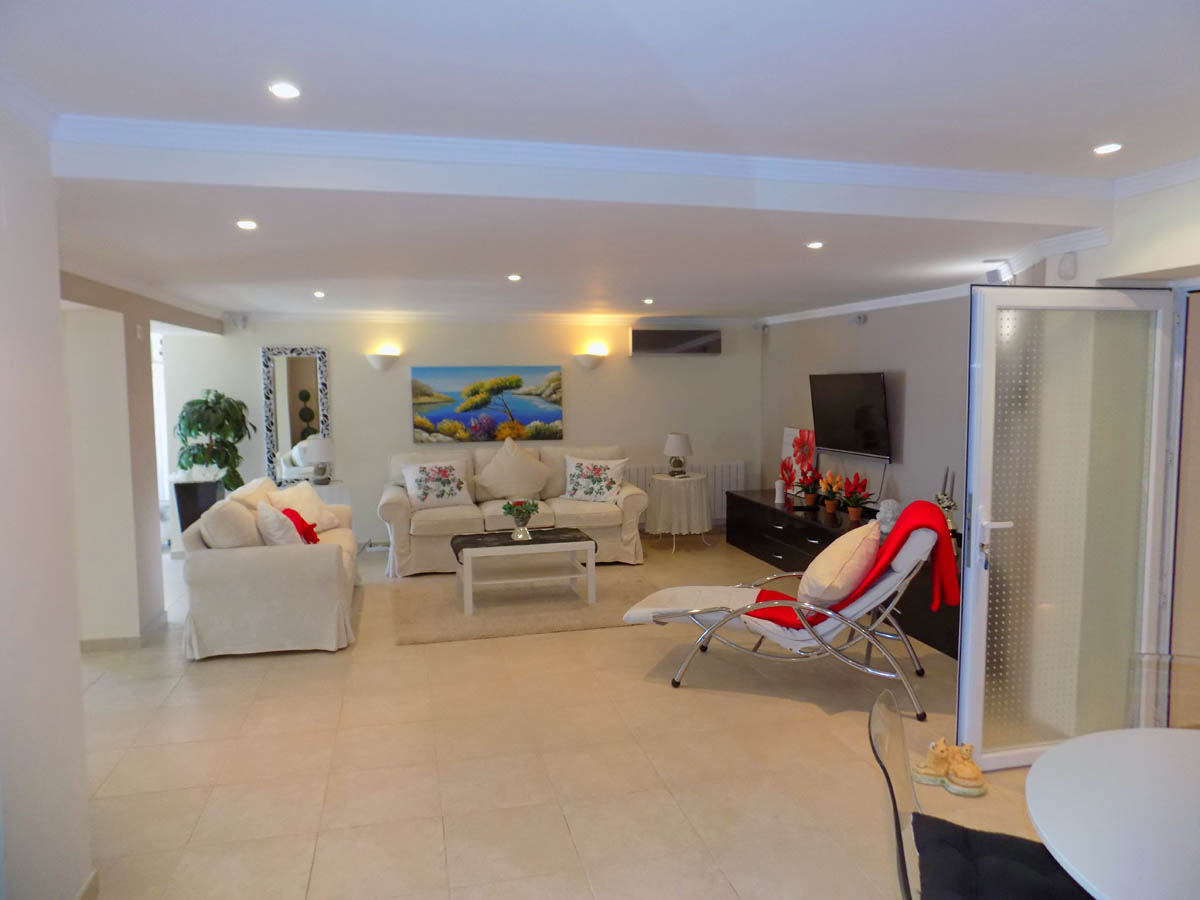 Spacious ground-floor living area featuring tiled flooring, recessed ceiling lighting, and comfortable seating. The room includes a TV unit and direct access to the garden.
