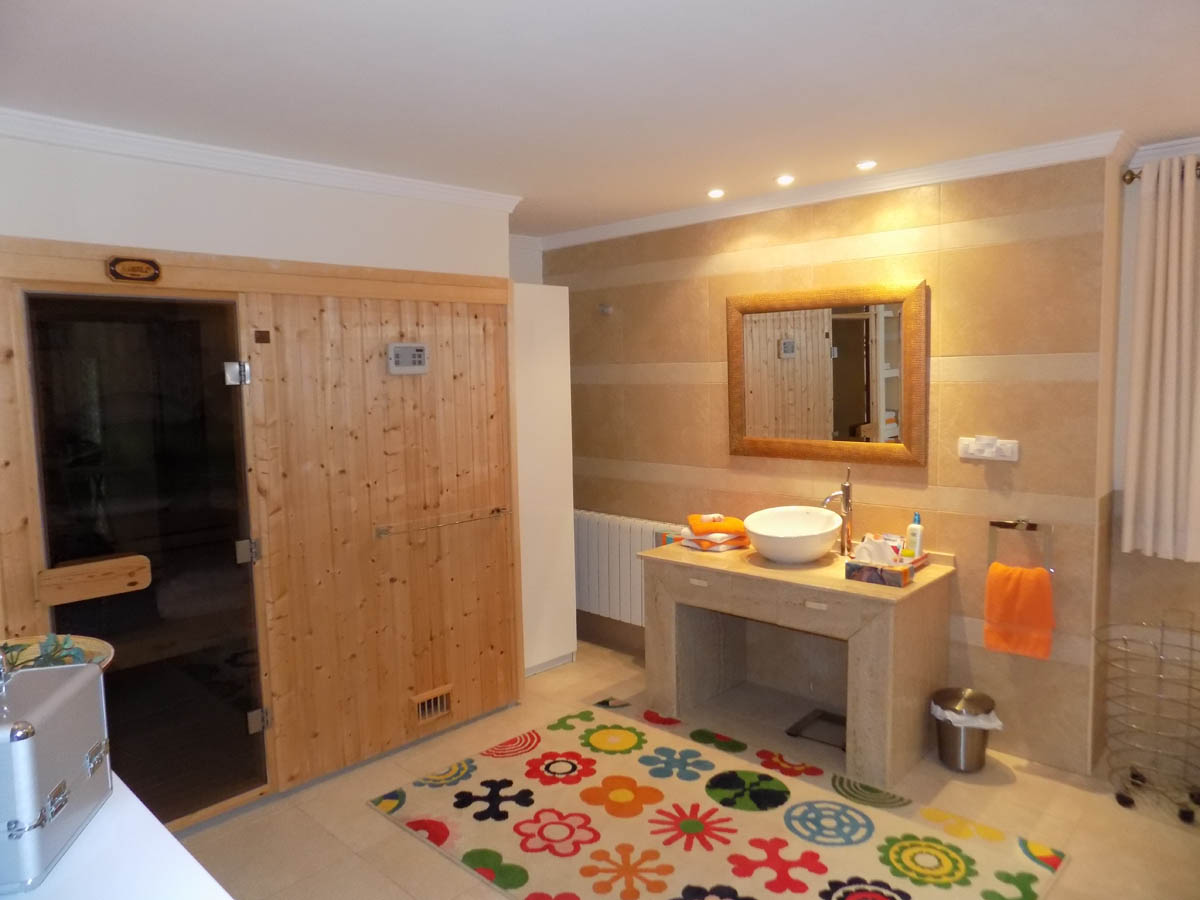Wellness area featuring a built-in wooden sauna, a stone vanity with a vessel sink, and warm-toned tiled walls with recessed spotlighting.