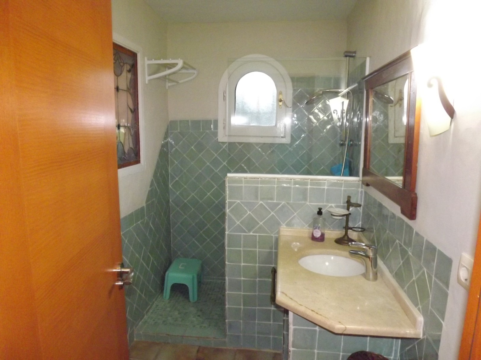 Bathroom featuring green diagonal tiling, a marble vanity with an integrated sink, and a walk-in shower with an arched window.