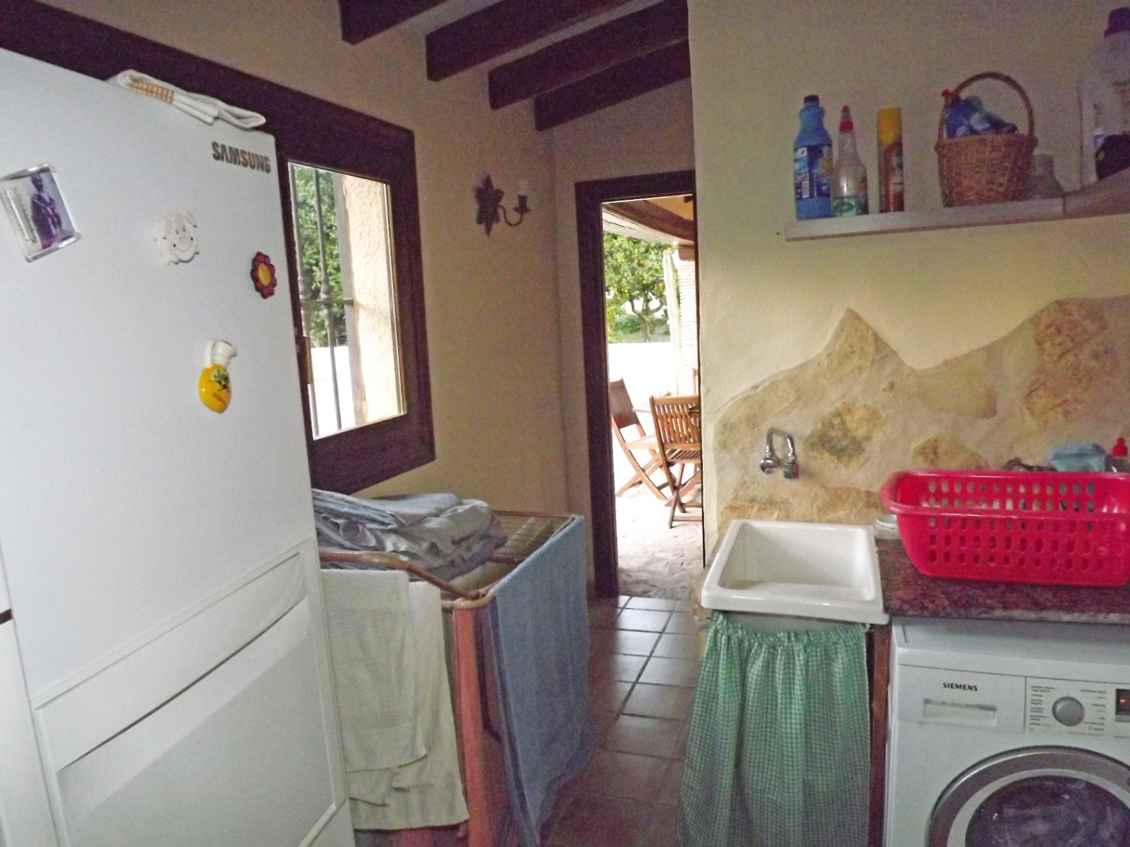 Functional utility room featuring exposed wooden beams, a Siemens washing machine, and direct terrace access. Includes natural stone wall accents and tiled flooring.