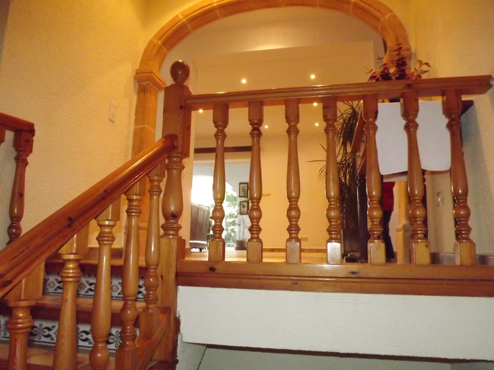 Interior staircase featuring a turned wood balustrade, decorative tiled risers, and a natural stone archway framing the entrance to the upper level.