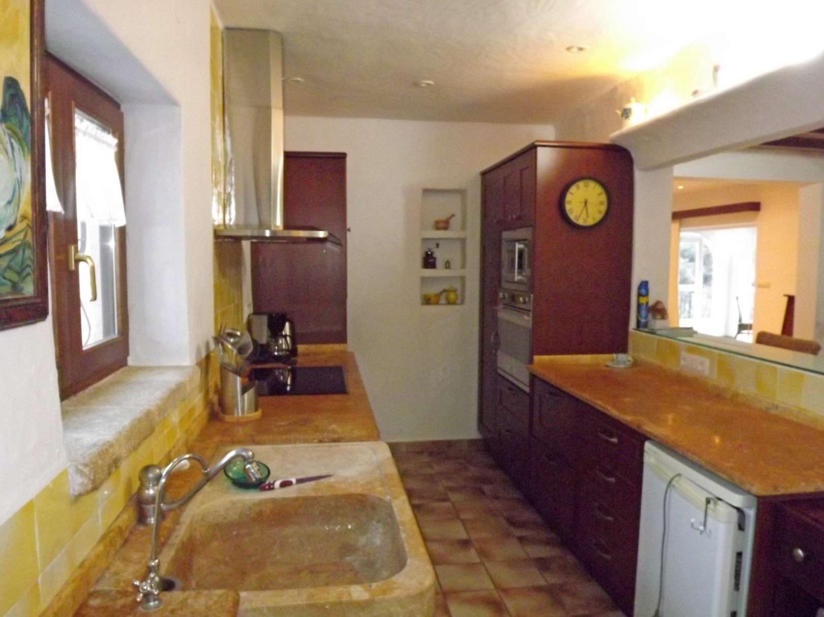 Rustic kitchen featuring a carved stone sink, dark wood cabinetry, and yellow tile accents. It includes integrated appliances and a pass-through to the living area.