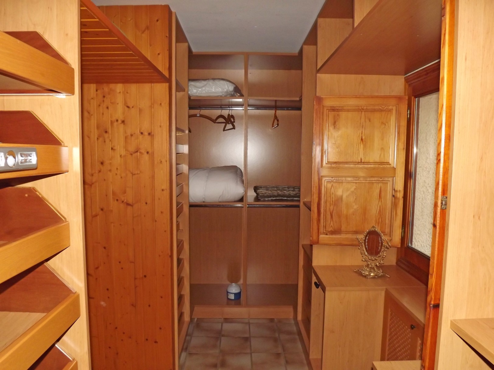 Walk-in closet featuring custom wood shelving, hanging rails, and tiled flooring. The space includes a functional window with a traditional wooden shutter for natural light.