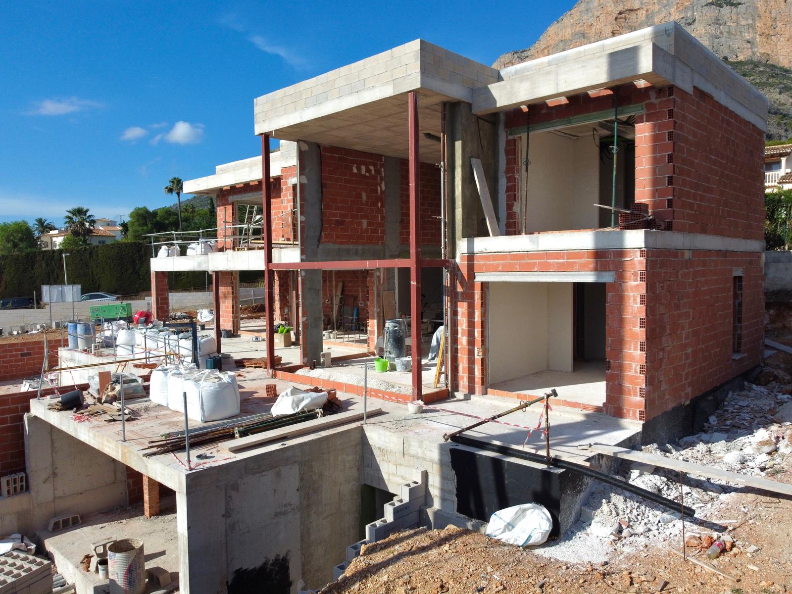 Current construction phase of the villa, featuring the brick structure, concrete slabs, and steel beams set against the Montgó mountain backdrop.