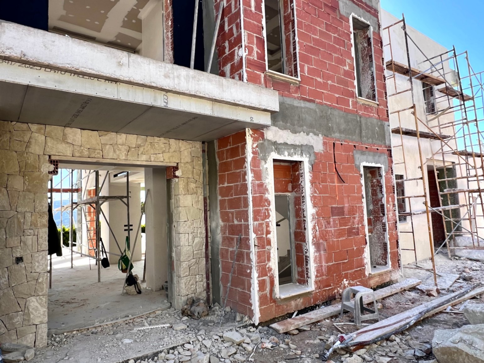 Current construction progress featuring red brick walls, natural stone cladding accents, and concrete structural elements with exterior scaffolding.