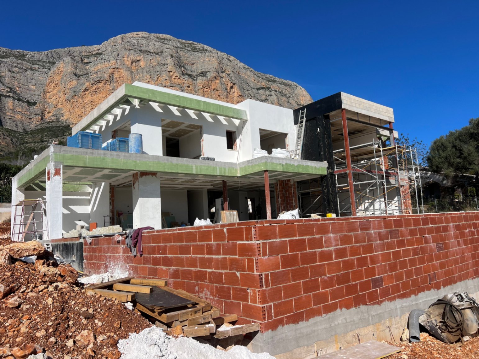Exterior view of the villa under construction against the Montgó mountain, featuring the two-level concrete structure and spacious terrace layouts.