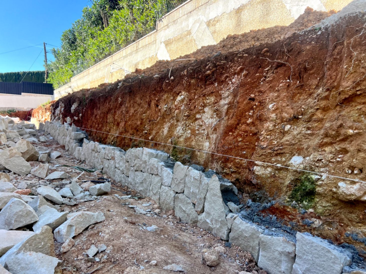 Initial construction phase featuring the manual assembly of a natural stone retaining wall against an excavated earth bank on the plot.